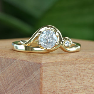 Handmade 18ct gold Art Nouveau engagement ring with icy diamond and accent diamond on natural wooden surface.