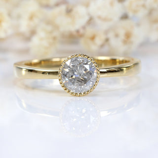 Close-up of 18ct gold salt and pepper diamond solitaire ring on pale floral background