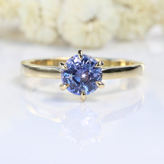 18ct gold Lavender blue sapphire engagement ring on soft white floral backdrop.