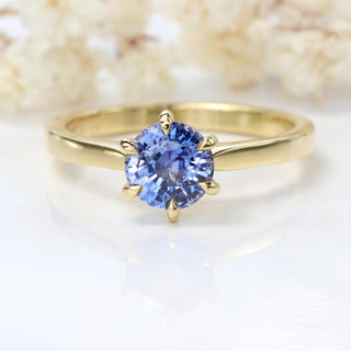 Natural unheated lavender sapphire solitaire engagement ring photographed on soft floral background.