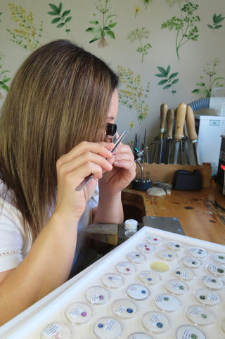 Jewellery designer Lilia Nash examining loose gemstones with a loupe. Jewellery bench and floral paper background