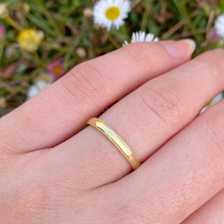 Sustainable 18ct gold 2.5mm wide wedding band with a hand engraved milgrain border. Shown being worn on the hand with daisy backdrop.
