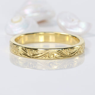 18ct gold wedding band with a floral scroll pattern engraved around the  band, on a grey background
