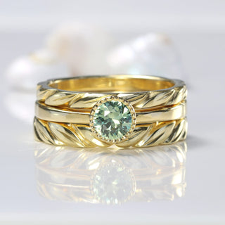 Green sapphire solitaire ring with carved leaves wedding bands, on reflective surface 