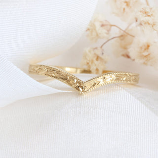 Gold wishbone ring with a textured design on a white fabric background