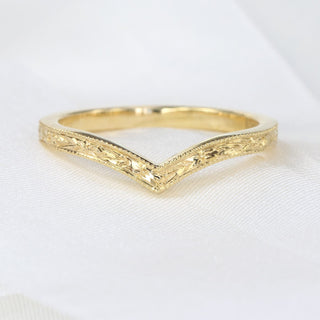 A gold wishbone ring with a textured surface shown on white fabric