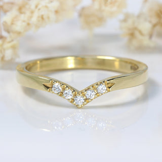 18ct gold wishbone wedding band with pave set diamonds at the front on a white surface with flowers
