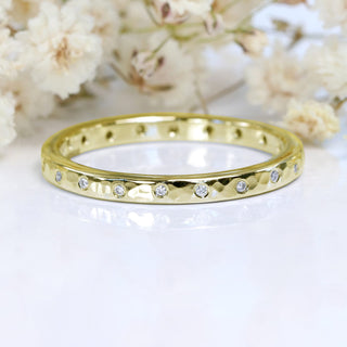 18ct gold slim hammered wedding ring set with twenty diamonds, on a white surface with flowers