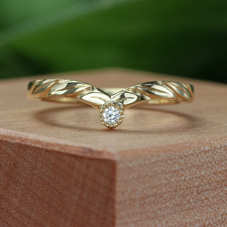 A 18ct gold wishbone style wedding ring with a central diamond accent and engraved leaf patterns on the band, displayed on a wooden block.
