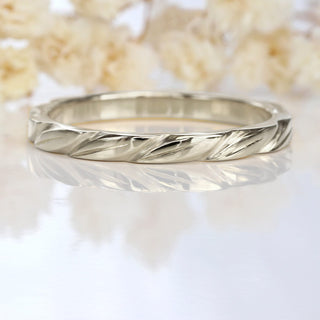 Lilia Nash signature white gold wedding ring with leaves around the band on a white background with flowers
