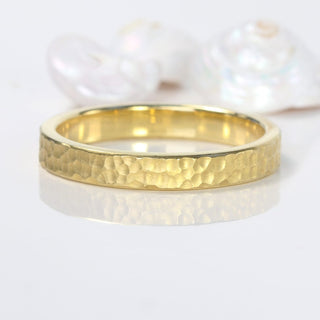 3mm wide 18ct gold wedding band with a flat profile and hammered finish, on a reflective surface