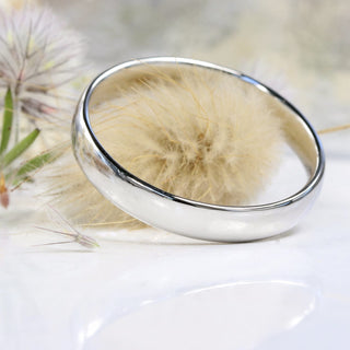 4mm wide Court shape 950 platinum wedding ring with polished finish, resting on a seedhead