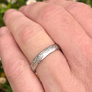 18ct palladium white gold men's wedding ring in a 4mm court profile. Hand engraved with an oak leaf pattern. Show being worn on the hand.