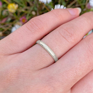 Hand engraved sustainable platinum wedding band in a 2.5mm wide court profile, with milgrain border. Shown being worn on the hand