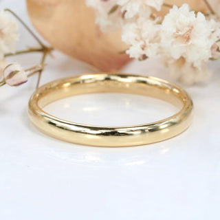 9ct gold 2.5mm wide court wedding band with polished finish on white background with flowers