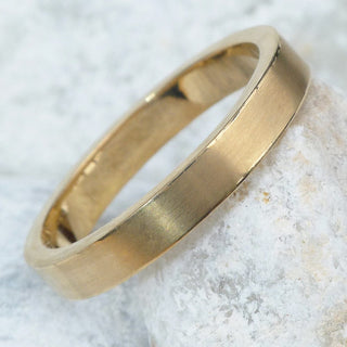 3mm wide 9ct gold wedding ring with matte finish resting on a rock