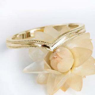 9ct gold wishbone wedding ring with a hand engraved milgrain border, resting on a yellow flower