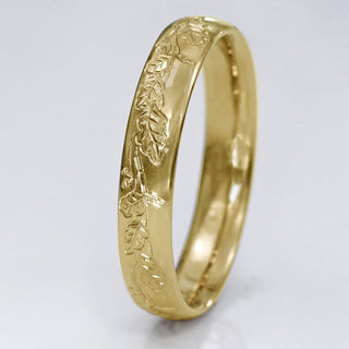 Front view of 9ct gold 4mm court wedding band with hand engraved oak leaves, on a white surface