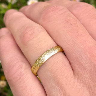 Sustainable solid 9ct gold 4mm court wedding ring with hand engraved oak leaf pattern. Displayed being worn on a man's hand.