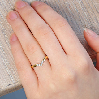 9ct gold wishbone wedding ring with pave set diamonds at the front. Worn on the hand, resting on a wooden surface
