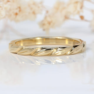 Slim 9ct gold wedding ring with hand engraved leaves around the band, on a white surface with flowers