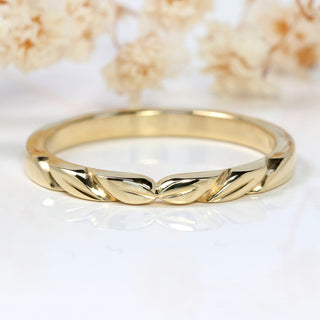 9ct gold slim wedding band with hand carved leaves at the front on a white surface with flowers