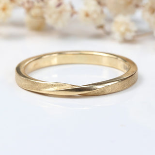 9ct gold ribbon twist wedding band with spun silk finish on a white surface with flowers
