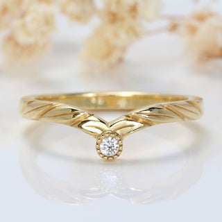 Solitaire diamond 9ct gold wishbone wedding ring with hand engraved leaves, on a white surface.