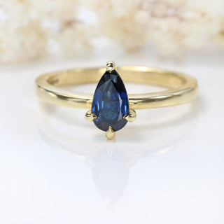 Angled view of pear cut blue sapphire engagement ring in 18ct gold