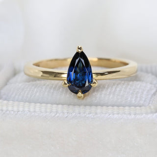 Pear cut sapphire engagement ring in 18ct gold photographed on cream fabric.