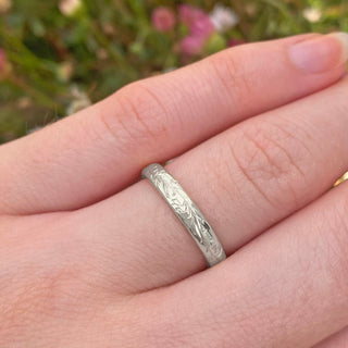 Sustainable platinum court wedding ring with hand engraved bluebell flowers around the 3mm wide band. Displayed being worn on the hand