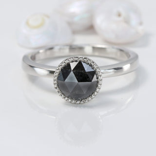 Black diamond platinum solitaire engagement ring on grey background with sea shells