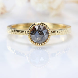 Close-up of 18ct gold salt and pepper diamond solitaire ring on pale background.
