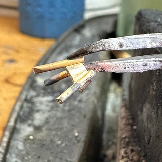 Pliers holding a gold setting used to make a trilogy engagement ring.