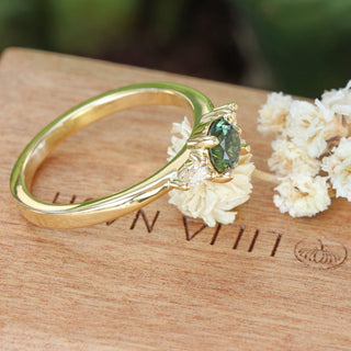 Top view of Bespoke 18ct gold dark green sapphire and diamond trilogy engagement ring on a branded wooden box with white flowers