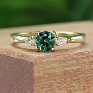 Bespoke dark green sapphire and diamond trilogy engagement ring on a wooden box with green background