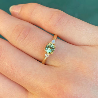 Green sapphire and diamond trilogy ring in 18ct gold, being worn on the hand with green background.