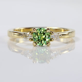 Green sapphire engagement ring in trilogy style, handmade  with fair trade sapphire and Canadian diamonds, on reflective grey background