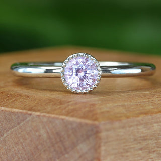 Handmade platinum pink sapphire solitaire engagement ring with milgrain bezel on wooden block.