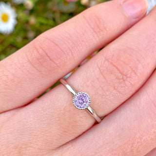 Petite solid 950 platinum solitaire engagement ring with a lilac pink sapphire within a bezel setting with milgrain detail. Shown worn on the hand