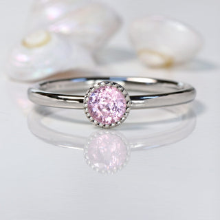 Petite pink sapphire platinum solitaire engagement ring on grey surface with sea shells