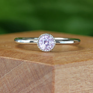 Handmade platinum pink sapphire solitaire engagement ring with milgrain bezel on wooden block.