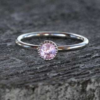Pink sapphire solitaire ring in platinum photographed on grey texture.