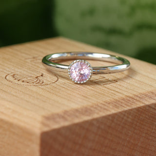Platinum pink sapphire ring photographed on wooden block with soft background.