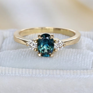 Parti sapphire trilogy engagement ring in handmade 18ct gold photographed on pale fabric.