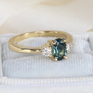 18ct gold trilogy engagement ring with natural Parti sapphire and diamonds photographed on pale fabric.