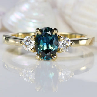 Teal sapphire and diamond trilogy engagement ring, with seashell background