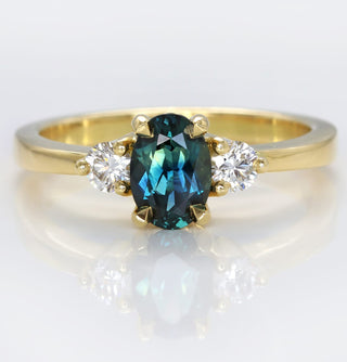Handmade 18ct gold Parti sapphire trilogy engagement ring with Canadian diamonds on reflective surface.