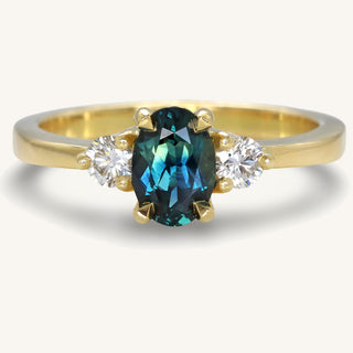 Handmade 18ct gold trilogy engagement ring set with a fair trade oval dark teal sapphire, flanked by natural white diamonds