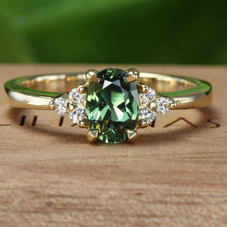 18ct gold cluster engagement ring with an oval green sapphire and side diamonds on a branded wooden box